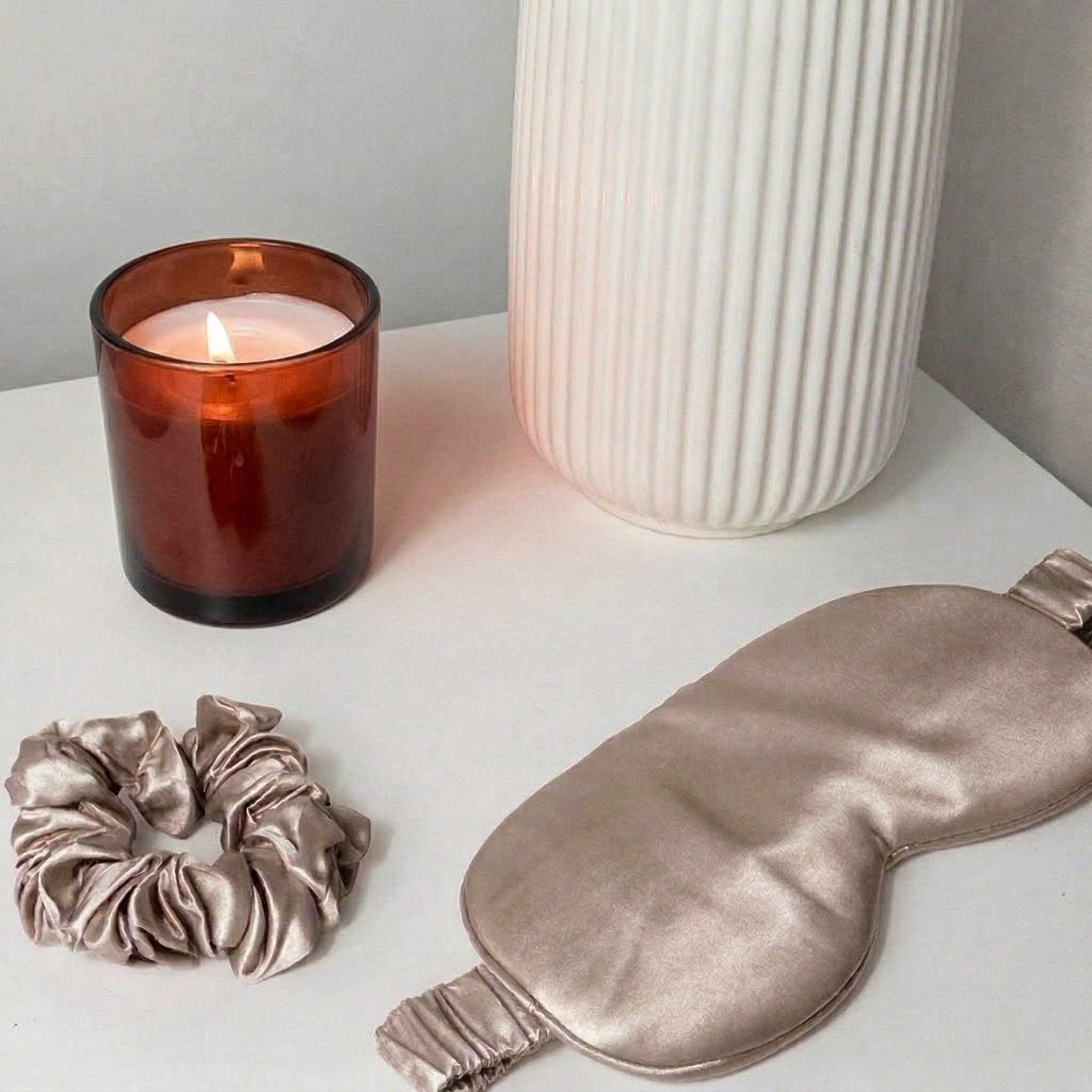 Seiden Schlafmaske und Scrunchie Set in Vintage Mauve auf weißem Tisch, neben Duftkerze