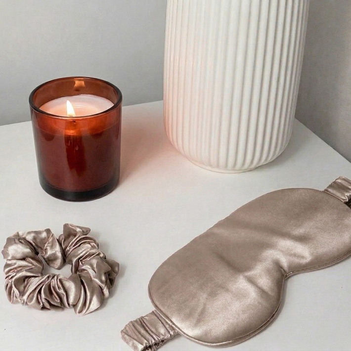 Seiden Schlafmaske und Scrunchie Set in Vintage Mauve auf weißem Tisch, neben Duftkerze