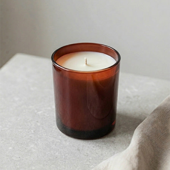 Mittelgroße Duftkerze mit cremefarbenem Wachs in rot-braunem Glas im minimalistischen Design